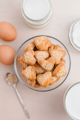 homemade heart shaped shortbread cookies with sesame seeds on a white table, eggs, sugar, flour and milk, flatley
