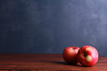 Two red fresh apples on brown wooden table against dark blue wall background with copy space....