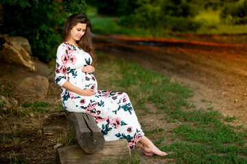 a pregnant woman in a dress walks in nature in the forest in summer