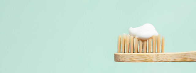 Banner with bamboo toothbrush with toothpaste on mint background with copy space. Close up view in...