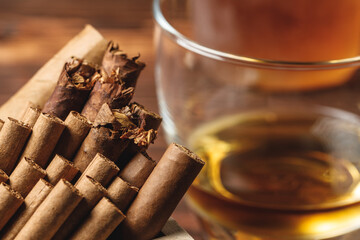 Glass of whiskey and rolled cigars on wooden table