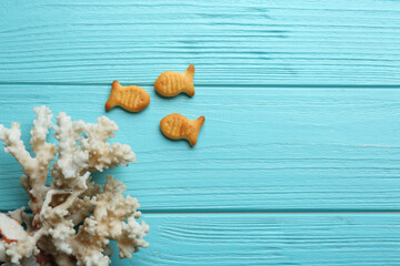 Delicious goldfish crackers and coral on light blue wooden table, flat lay. Space for text