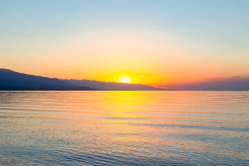 Dawn of the sun at sea. The rising sun behind the mountains. Kyrgyzstan.