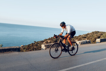 Man cyclist pedaling on a road bike outdoors in sun set