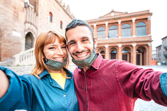Happy boyfriend and girlfriend in love taking selfie with face masks at old town tour - Wanderlust life style travel concept with tourist couple on city sightseeing vacation - Bright warm filter - Powered by Adobe