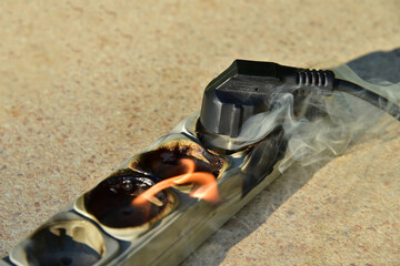Outlets with switche caught fire in room. Overloaded electrical current or short in device from many devices connected. Fire in socket of electric circuit causing. Burned and smoked plug with wire