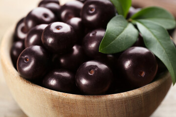 Tasty acai berries and green leaves in wooden bowl, closeup