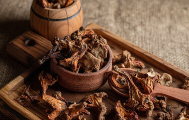 Dried chanterelle mushrooms, on a wooden board with a wooden spoon and a wooden barrel
