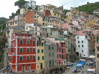 Fototapeta na wymiar Riomaggiore, Italy - 08/31/2020: Beautiful photography of the countryside from Cinque Terre, Italy. Grey sky, colourful houses, grape coltivation from the mountains, and some small waves from the sea.