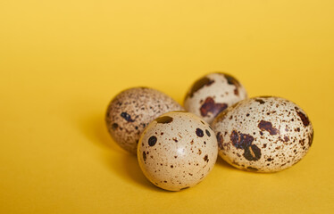 Four quail eggs lie next to each other on a yellow background