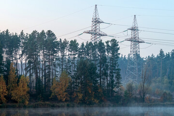 Power line in the cleared area of the forest. Steel electro masts with wires by the lake.