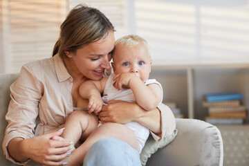 Horizontal medium portrait of attractive Caucasian woman wearing casual outfit sitting with her baby on lap, copy space