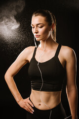 Obraz premium Slim sports woman with earphones on the black studio background