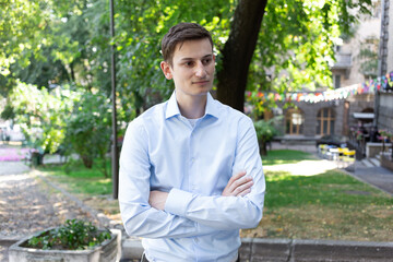 Portrait of young smiled man in a blue shirt on the city with a trees on the background. The man in conversation, listens and speaks. American or European appearance
