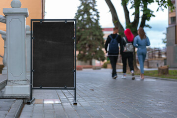 empty vertical chalkboard in metal frame stands on tiled footpath at city street people walking background