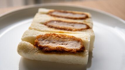 Pork cutlet tonkatsu sandwich or katsu sando is a popular convenient snack food in Japan found in stores, subway and mall markets sometimes packaged in wooden boxes. Close-up selective focus on plate.