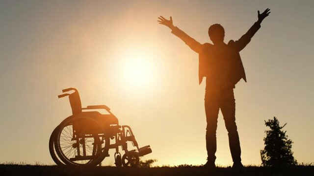 Happy man near wheelchair raises his hands up