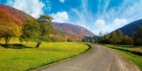 country road winding through the valley. wonderful autumn landscape in mountains. forest on hills in colorful foliage. sunny weather with fluffy clouds on the sky