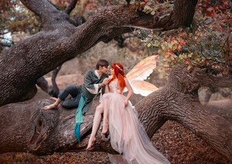 Young couple in love. A man and a woman are hugging on a huge tree. Themed creative wedding bright fantasy photography. Fairy woman in long pink dress with bright golden wings. A man in an elf costume - obrazy, fototapety, plakaty