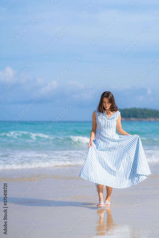 Wall mural full length of happy woman in beautiful blue summer dress posing and enjoying a walk on the sea beac