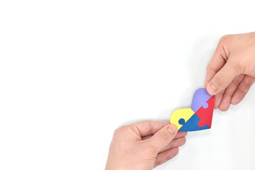 Male hands holding a colorful puzzle heart shape paper cutout. Top view flat lay in white background with copy space. World Autism awareness day, support and care concept.