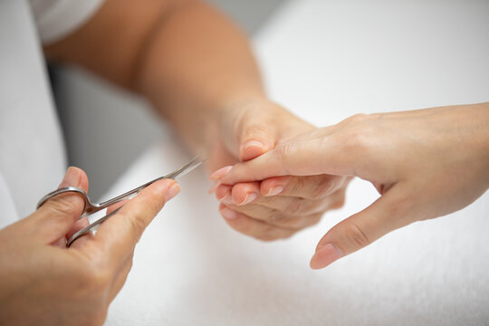 Close up of manicurist hands clipping client nails in a luxury spa. Young woman getting manicure treatment with hands kept on towel. Clipping nails, hand care and nailcare at beauty salon.