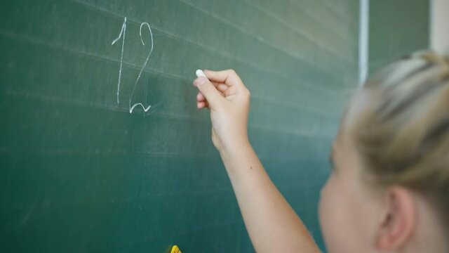 math lesson, schoolgirl at the blackboard writes numbers with white chalk in classroom at elementary school