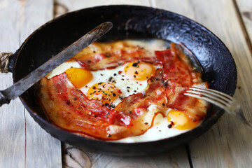 Selective focus. Scrambled eggs with bacon in a skillet on the table. Rustic style. English breakfast.