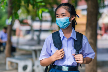 An Asian female student in white high school uniforms wearing the mask stand on the side of the road waiting for cars to go back home after school during the Coronavirus 2019 (Covid-19) epidemic.