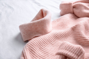 Pink warm sweater on white crumpled fabric, closeup