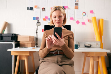 Mature Businesswoman With Mobile Phone Working At Desk In Start Up Creative Business