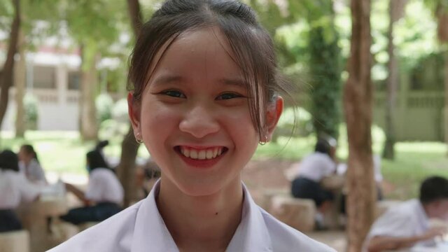 Slow motion of smiling Asian teen high school girl in white uniform standing in the school park.