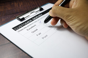 A man's hand is writing a pen to answer a customer satisfaction