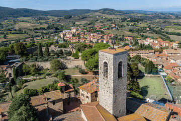 Fototapeta na wymiar Aerial view of medieval tower, houses and modern sports grounds in San Gimignano, Italy, and the surrounding fields, forests and mountains