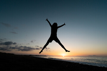 Fototapeta na wymiar A girl jumps for joy on the beach at dawn. Concept of happiness