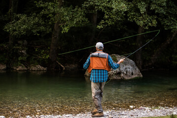 A fly fisherman fishing a trouts in mountain river
