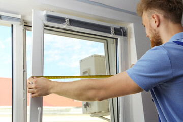 Naklejka na ściany i meble Handyman with tape measure installing window blinds indoors