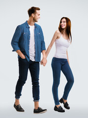 Happy lovers concept - young couple walking together, going somewhere, holding hands. Isolated over bright grey background. Caucasian models at full body length studio portrait image. Man and woman.