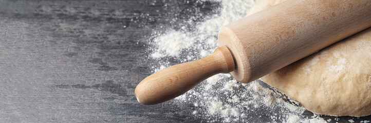 Dough with rolling pin and flour on table, closeup. Banner design with space for text