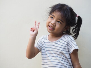 A cute and beautiful Asian kid girl wearing stripe shirt smiling and showing peace finger sign isolated on white. Happy natural expression. 