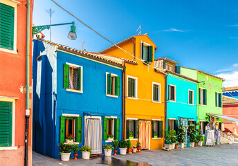 Fototapeta na wymiar Burano island colorful houses with multicolored walls, striped curtain on doors, shutter windows and flowers in pot, sunny summer day, Venice Province, Veneto Region, Northern Italy. Burano postcard