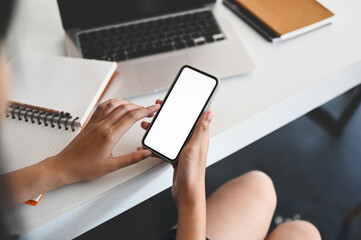The cropped image of a woman is using mockup smartphone at the white working desk.