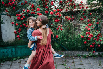 mom spins her daughter in an embrace in the park near red roses
