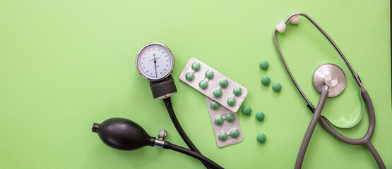 Blood pressure meter, medical stethoscope and medicine on pastel green background, close up view.
