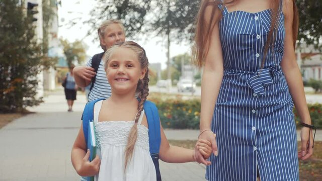 mom and daughter go to school. happy family school education concept. schoolgirl with mom go hand in hand to school on footpath in the park. little girl with a briefcase time lifestyle to study