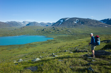 Fototapeta premium Hiking in Swedish Lapland. Man traveler trekking alone Nordkalottruta Arctic Trail with view of Lake Alisjavri in northern Sweden. Mountain nature of Scandinavia in summer sunny day