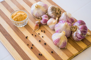 A beautiful and large garlic lies with peppercorns and garlic seasoning on a brown wooden board.