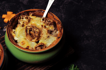  Baked potatoes with mushrooms in a clay pot on a black background