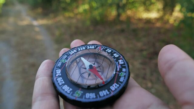 Extreme close-up of a transparent modern compas in the forest background. Concept of travel, adventure, expedition