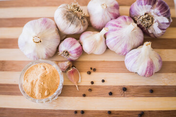 A beautiful and large garlic lies with peppercorns and garlic seasoning on a brown wooden board.